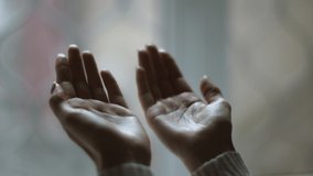 Close up shot of female palms against window, unrecognizable muslim lady praying to God at home, gesturing hands up, slow motion