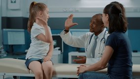 African american medic giving highfive to little child after successful checkup examination. Cheerful kid and doctor celebrating teamwork at consultation appointment with mother in office. - Powered by Shutterstock - Get 15% off with code: PIKWIZARD15