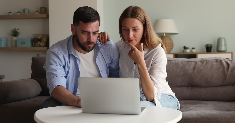 Young man woman in love cuddle on sofa play online game using laptop discuss lottery numbers combination feel excited after getting victory. Millennial couple overjoyed with buying item at web auction Royalty-Free Stock Footage #1085566931