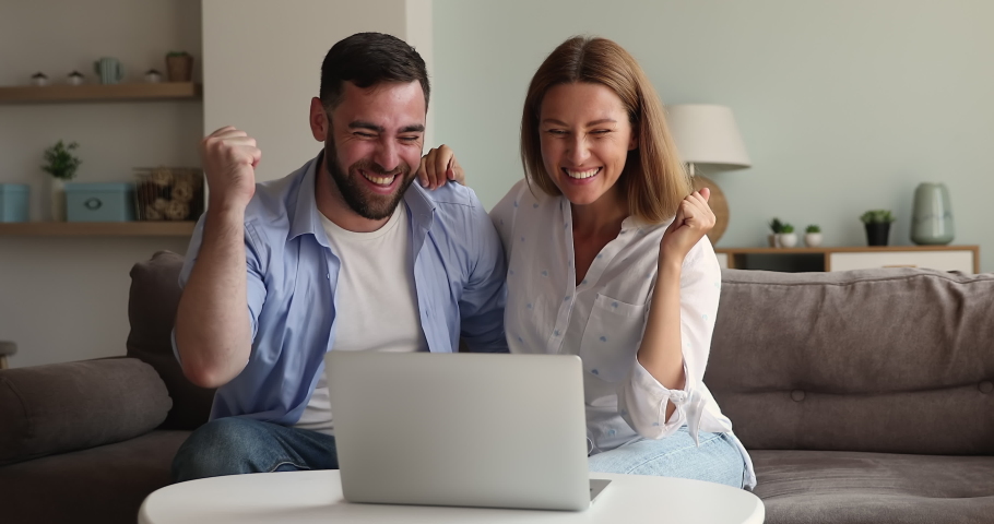 Young man woman in love cuddle on sofa play online game using laptop discuss lottery numbers combination feel excited after getting victory. Millennial couple overjoyed with buying item at web auction Royalty-Free Stock Footage #1085566931