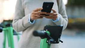 Woman using app on smartphone to unlock electric scooter on the street. - Powered by Shutterstock - Get 15% off with code: PIKWIZARD15