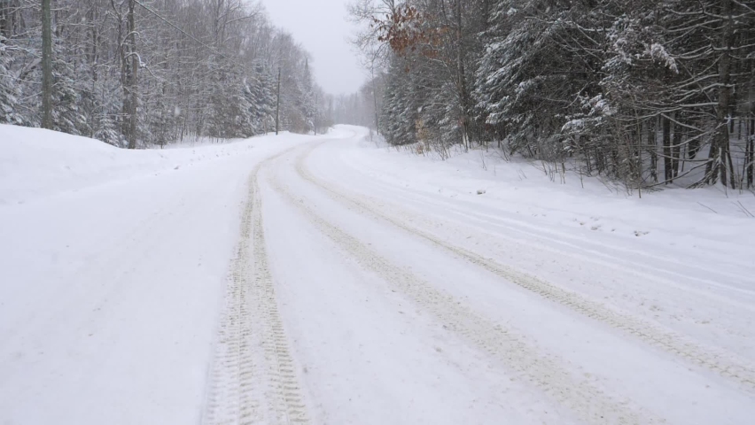 Tire tracks on curvy rural snow-covered winter road. Slow motion snow falling. Haliburton, Ontario, Canada. 
 Royalty-Free Stock Footage #1085567516