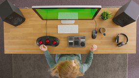 Overhead view of female video editor putting on wireless headphones and working at computer with green screen in creative office - shot in slow motion