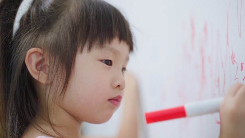 Asian young sibling kid girl enjoy paint on white wall in living room. Little adorable children having fun drawing and coloring art picture with hapiness enjoy creativity activity on holiday at home.