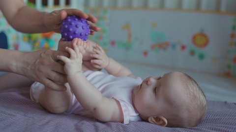 Female hands massage a child with a rubber ball. The child is lying on his back with his legs to top, and mom's hands doing massage to a baby.