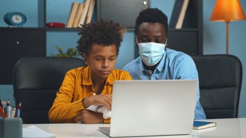 Father and son communicating with pediatrician on pc at home. African man in safety mask with sick son consulting doctor online on laptop. Healthcare and telemedicine concept