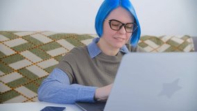 Focused young woman typing on computer. Beautiful female with dyed blue hair working on laptop at home in 4k stock video clip. Millenial person doing distant freelance work on notebook pc and internet
