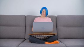 Millenial woman learning online. Individual white person with dyed blue hair working on laptop computer at home during lockdown. Caucasian female doing distant work on notebook connected to internet