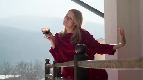 Young woman drinking hot tea at the balcony of chalet during winter.