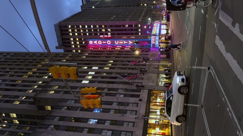 NEW YORK, USA - OCTOBER, 24, 2021: Vertical video. Radio City Hall. 6th avenue street in the NYC city at night. Road, people, traffic, intersection. Buildings in midtown Manhattan, traffic lights.
