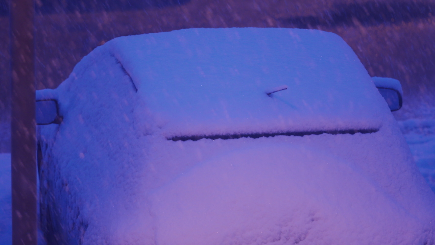 Parked cars covered with snow at dusk under a street lamp in parking lot in winter. Heavy snowfall on city streets. High quality 4k footage