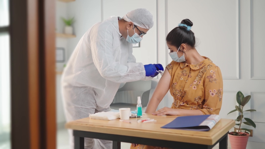 A doctor injecting vaccination in arm of a young Indian Asian female while both faces are covered with protective masks at modern clinic or hospital amid coronavirus or COVID 19 epidemic or Pandemic Royalty-Free Stock Footage #1085597459