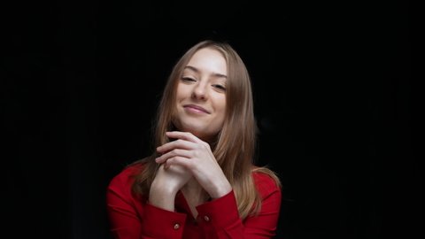 Portrait of a young girl coquettishly looking at the camera and drawing a heart sign on the misted glass. Model girl in a red blouse posing on a black background in the studio. Close up. Slow motion.