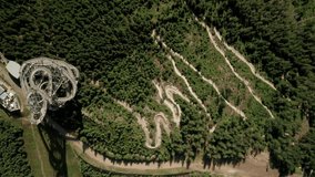 Aerial drone point of view of a sky walk tower attraction in Dolni Morava, Czech Republic and a nearby MTB bicycle trail. Mountain bikers are riding down the winding trail. Camera is zooming in slowly