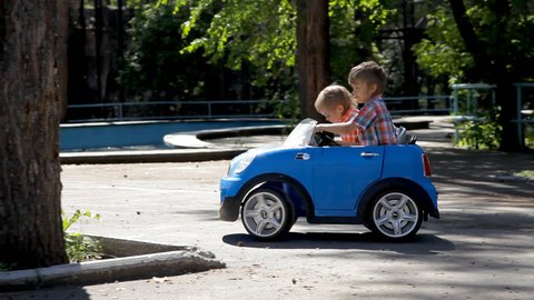 Two little boys riding a big toy car.
