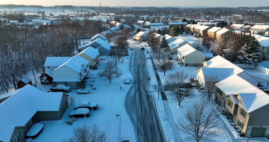 Residential homes in USA covered in fresh winter snow. Plowed street through neighborhood community in America. Descending aerial.