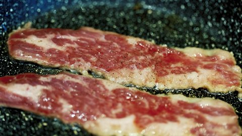 Close-up view of bacon slices in frying pan.
