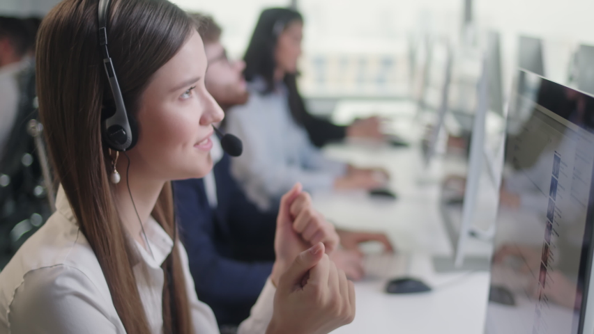 Close Up Portrait Woman of a Technical Customer Support Specialist Talking on a Headset while Working on a Computer in a Call Center. Diverse group of workers talks on sale hotline. Royalty-Free Stock Footage #1085611145