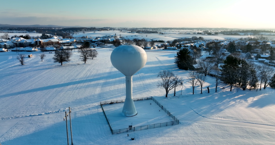 Water tower in rural America. Municipal supply of fresh water for homes in small town USA. Aerial orbit in winter snow.