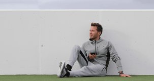 Fitness man using phone app on break relaxing outdoors. Active lifestyle young adult holding smartphone watching online video or texting sms messages. Sweatsuit and sweatpants