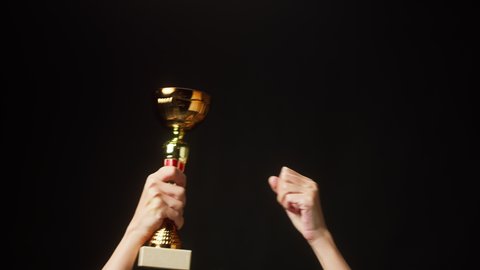 Professional sportsman winner holding gold cup close-up. Athlete raising world cup on black background, having first place. Award and victory, winning the championship.
