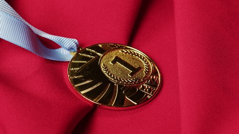 Gold medal with ribbon on red background close-up. The first place. Award and victory, winning the championship. 