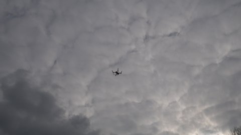 A drone hanging still in the sky in a cloudy day.