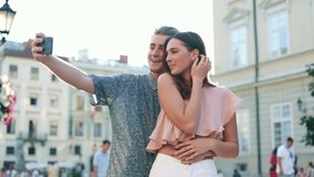 Young couple in love standing on street and taking pictures, selfie, photos. People using smartphone to shoot video, posing for camera outdoors. Photography, technology, gadget
