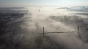Drone video in 4k as the morning fog covers the river and creeps under the suspension bridge