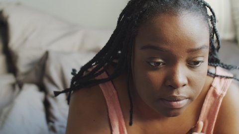 High angle view close-up shot of young Black woman having depression sitting on bed in morning thinking about something