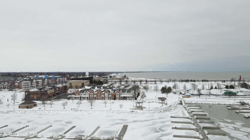 Aerial view toward Lake Michigan. Boats in dry dock. Ice and water in the empty boat slips, Seagulls flying in the sky. Multistory buildings and park. 