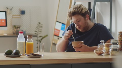 Young Caucasian man spending morning at home eating oats with milk for breakfast and chatting on phone with someone
