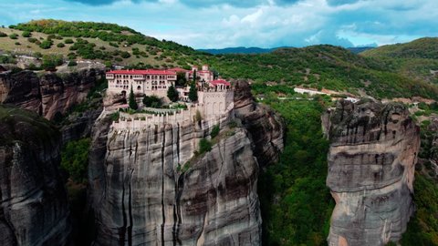 Meteora Greece Monastery. Drone flies among the mountain rocks where ancient Monastery located. Landscape scenery with green hills, rocks, and old caste-temple on it. Greece, cloudy autumn day.