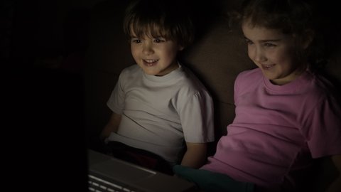Boy and Girl Watch Cartoon on Laptop on Living Room. Concept Video Game, Entertainment, Emotions, Family. Children Brother and Sister Watching TV. Portrait Сute Little Kids While Watching TV on Laptop