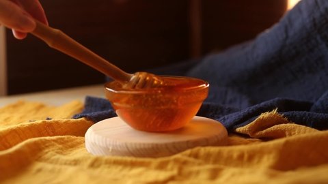 A wooden honey spoon is dipped into thick sweet delicious honey in a bowl. Drips off a spoon. Sugar substitute. Natural sweetness.
