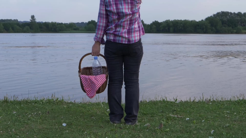 Woman stands by lake shore with vintage picnic basket wide slow motion shot selective focus 