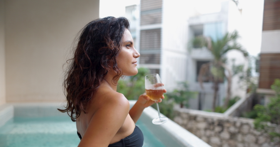 Beautiful brunette woman in pool drinking glass of champagne in slow motion. Attractive woman with wavy hair enjoying sparkling golden drink with blurry background. People in holidays | Shutterstock HD Video #1085638337