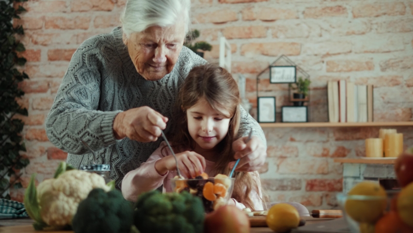 Grandma and granddaughter mix fruit salad together in the kitchen. The concept of a happy vegetarian family Royalty-Free Stock Footage #1085639963