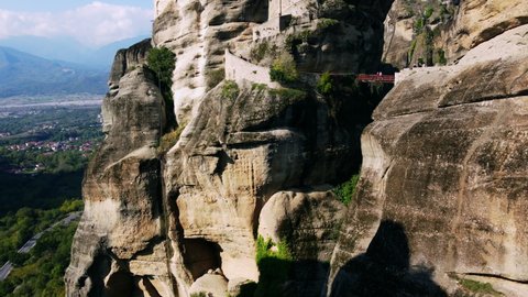 Meteora Greece Monastery. Drone flies among the mountain rocks where ancient two Monasteries located. Landscape scenery with green hills, rocks, and old town below.