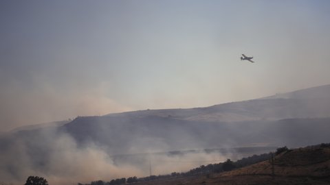 Rescue firefighting aircraft flying over the dry grassland that is on fire due to the heat wave. Global warming, climate change concept.