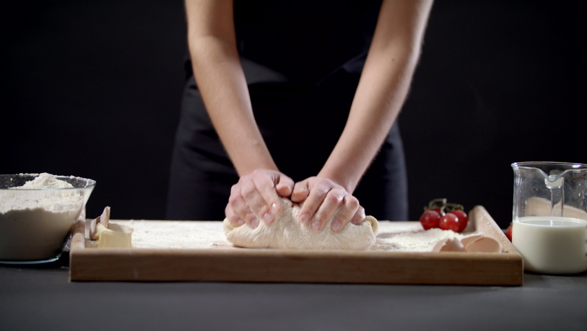 Closeup Shot Of Female Hands Of Baker Kneading Dough In Flour On Wooden Board On Table In Bakery Shop, Woman Making Bread Using Traditional Recipe At Home On A Black Background Slow Motion Royalty-Free Stock Footage #1085641475
