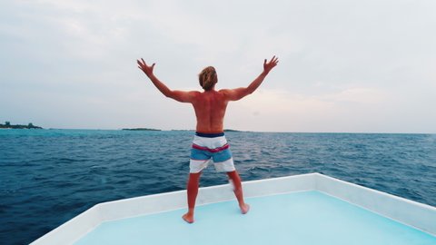 Boat trip in Maldives. Man stands on the roof of a moving boat with extended hands