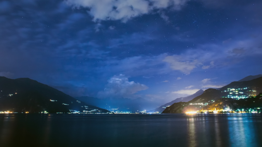 Timelapse of Lake Como at night. High quality 4K footage. The lights of the villages are reflected in the water, the clouds move in different directions and change shape, boats and ships sail