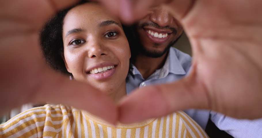 Affectionate African American couple in love enjoy romance in life look at web camera through heart shape of united palms. Romantic spouses shoot self video record greeting with Valentine Day. Closeup Royalty-Free Stock Footage #1085646224