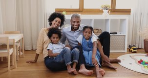 Friendly Black family portrait mom dad elder tween daughter younger son sit on warm floor at children room look at camera cuddle wave hands. Happy smiling couple with kids make video call record vlog