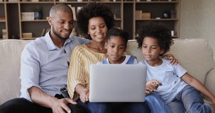 Black married couple foster parents with adopted kids elder daughter younger son relax on sofa use laptop watch video movie play game. Happy family of 4 rest at living room browse social media on pc