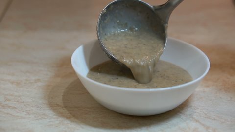 Preparation of mushroom puree soup at the kitchen, process of pouring food at white bowl using silver metal ladle, healthy eating