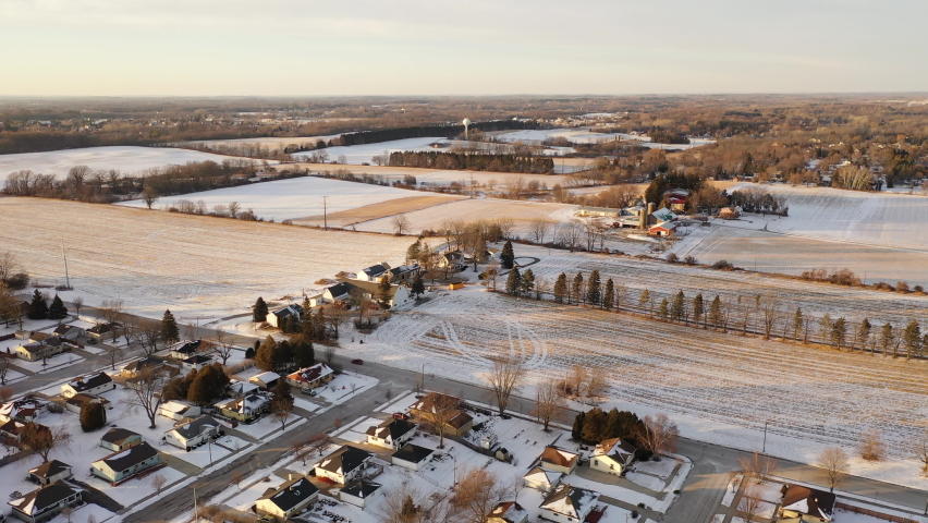 Aerial above houses covered in snow in a small town in USA in winter, farm and agricultural fields in  background. Suburban neighborhood in Midwest USA. Establishing shot of America