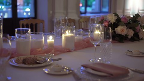Served table in a restaurant for dinner, lunch or celebration. White tablecloth, plates, napkins and glasses, chairs. Holiday indoors. Empty with no people and food. Decorated with flowers for wedding
