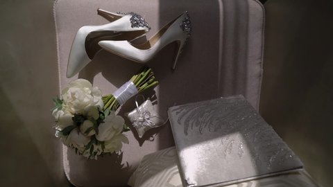 Wedding morning of the bride. White shoes with heels, a bridal bouquet of roses and wedding rings on chair.